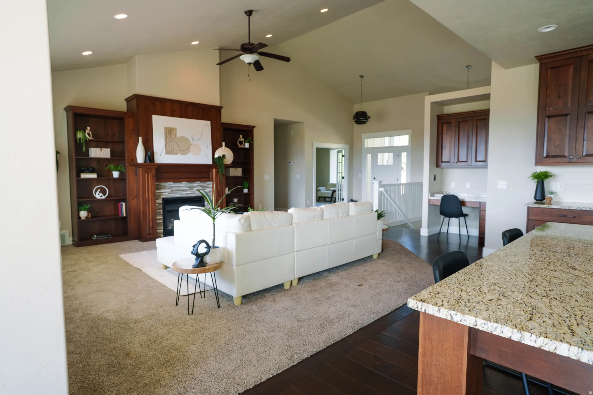 Living area featuring a stone-surround fireplace with a wood mantle, built-in shelving, vaulted ceilings with recessed lighting, and a ceiling fan