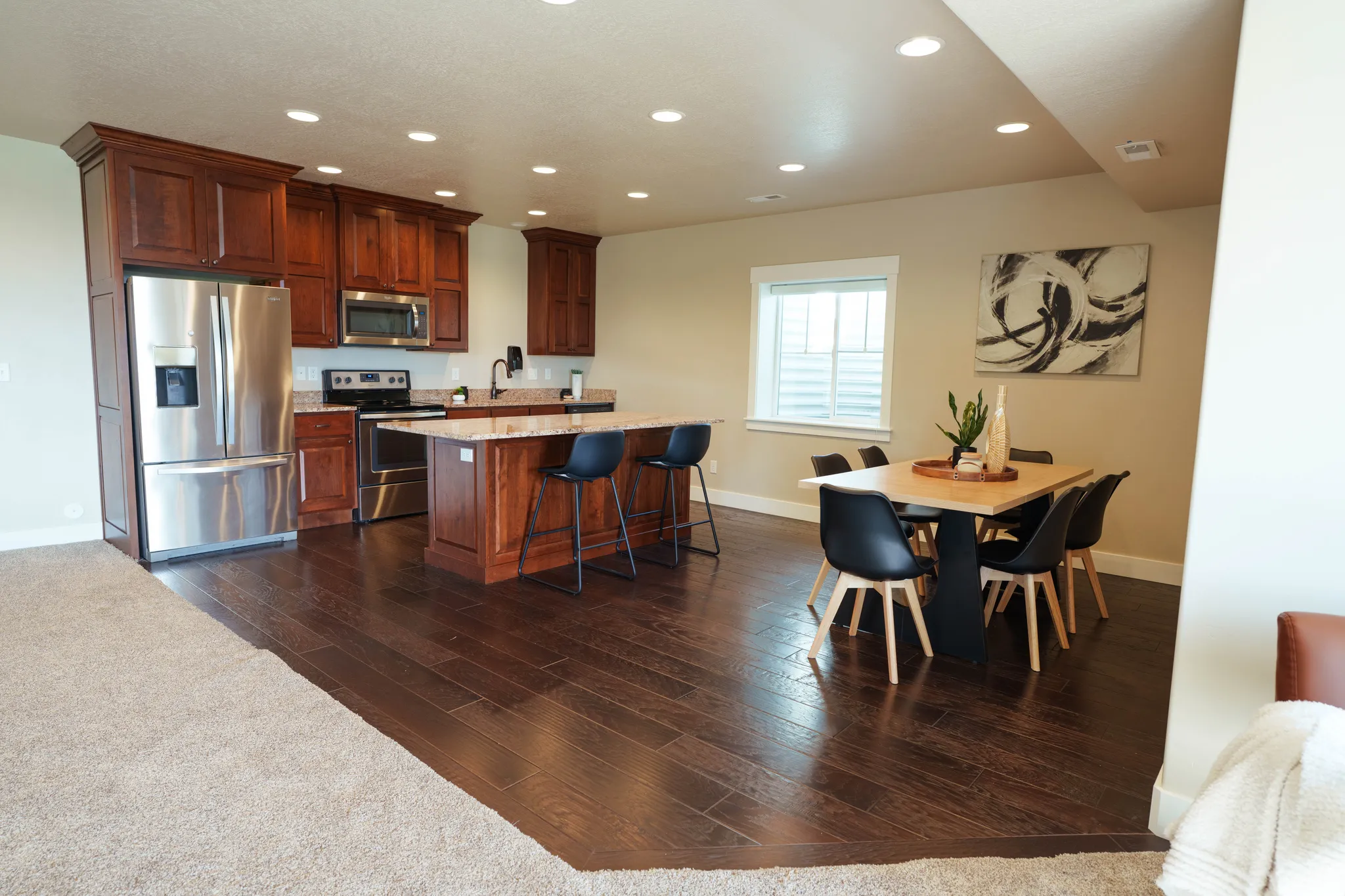 Open-concept kitchen and dining area featuring rich wood cabinetry, stainless steel appliances, a granite-topped island, wood-finish flooring, and recessed lighting