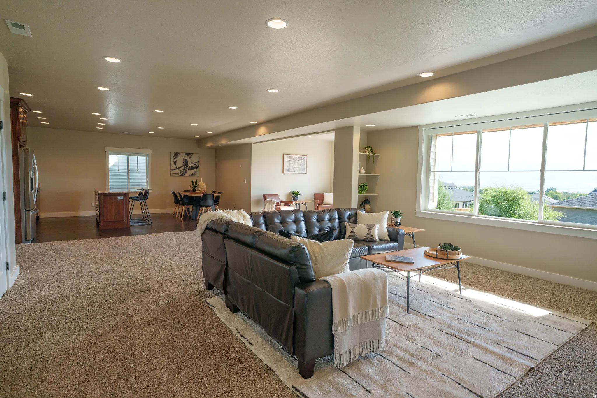 Open-concept living area with expansive windows, recessed lighting, carpet flooring, a dining area with wood-finish flooring, and built-in shelving