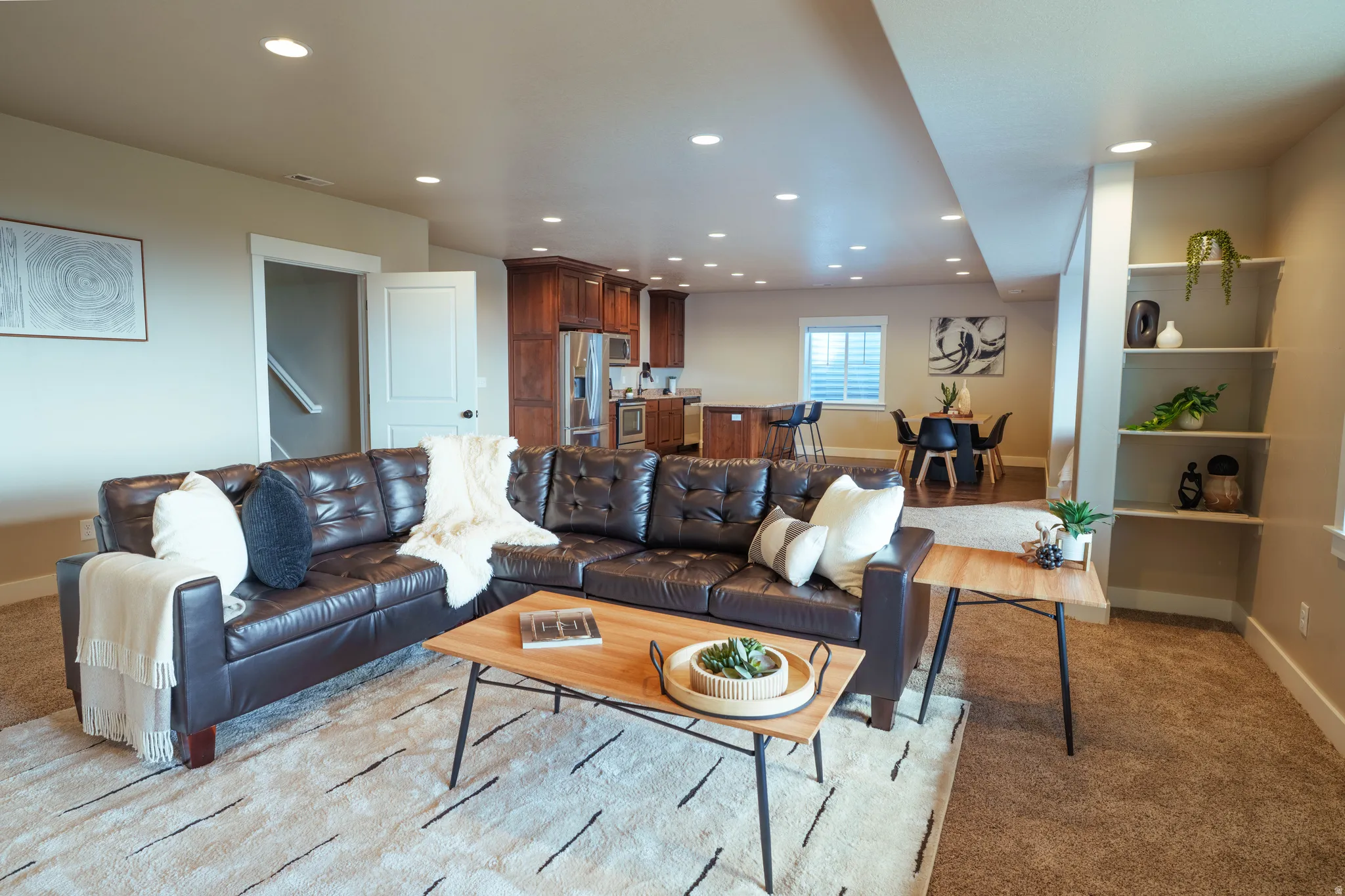 Open-concept living area featuring recessed lighting, a neutral color palette, built-in shelving, a kitchen with dark wood cabinetry, and a dining area with a window