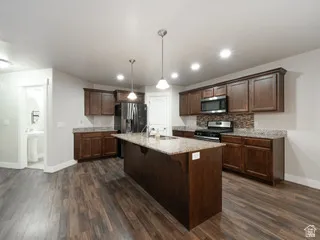 Kitchen featuring a central island with dual pendant lighting, wood-finish flooring, dark wood cabinetry, and a mosaic tile backsplash