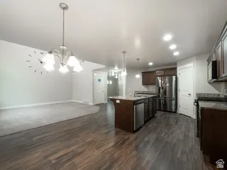 Open-concept living area featuring wood-finish flooring, a kitchen island, stainless steel appliances, recessed lighting, and a chandelier