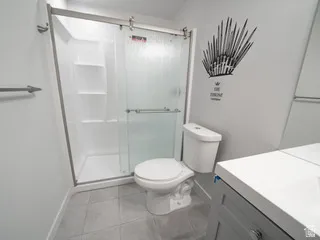 Bathroom featuring a white toilet, gray tile flooring, and a glass-enclosed shower with built-in shelving