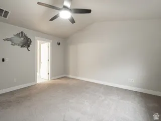 Spacious room featuring vaulted ceilings, a ceiling fan with integrated lighting, light gray wall paint, white trim, and plush carpeting