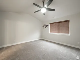 Vaulted ceiling with a ceiling fan, neutral wall paint, carpet flooring, a window with horizontal blinds, and white baseboards