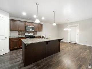 Open-concept kitchen featuring dark wood cabinetry, granite countertops, a mosaic tile backsplash, and stainless steel appliances