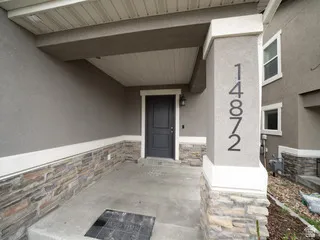 Stucco exterior with stone veneer detailing, covered porch entry, dark paneled door, and modern address numbering