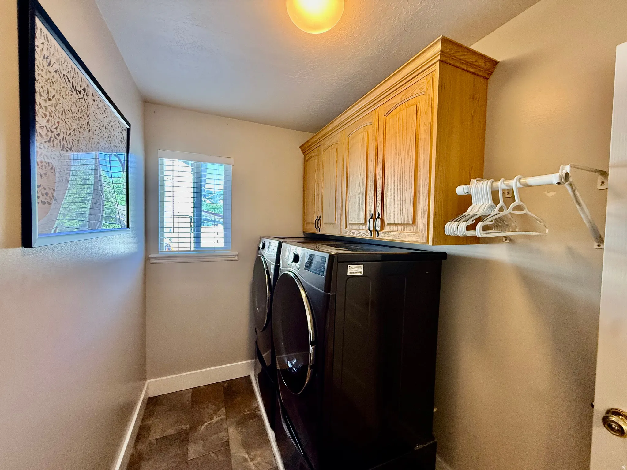 Dedicated laundry space featuring upper wood cabinetry, a window with blinds, and durable tile flooring