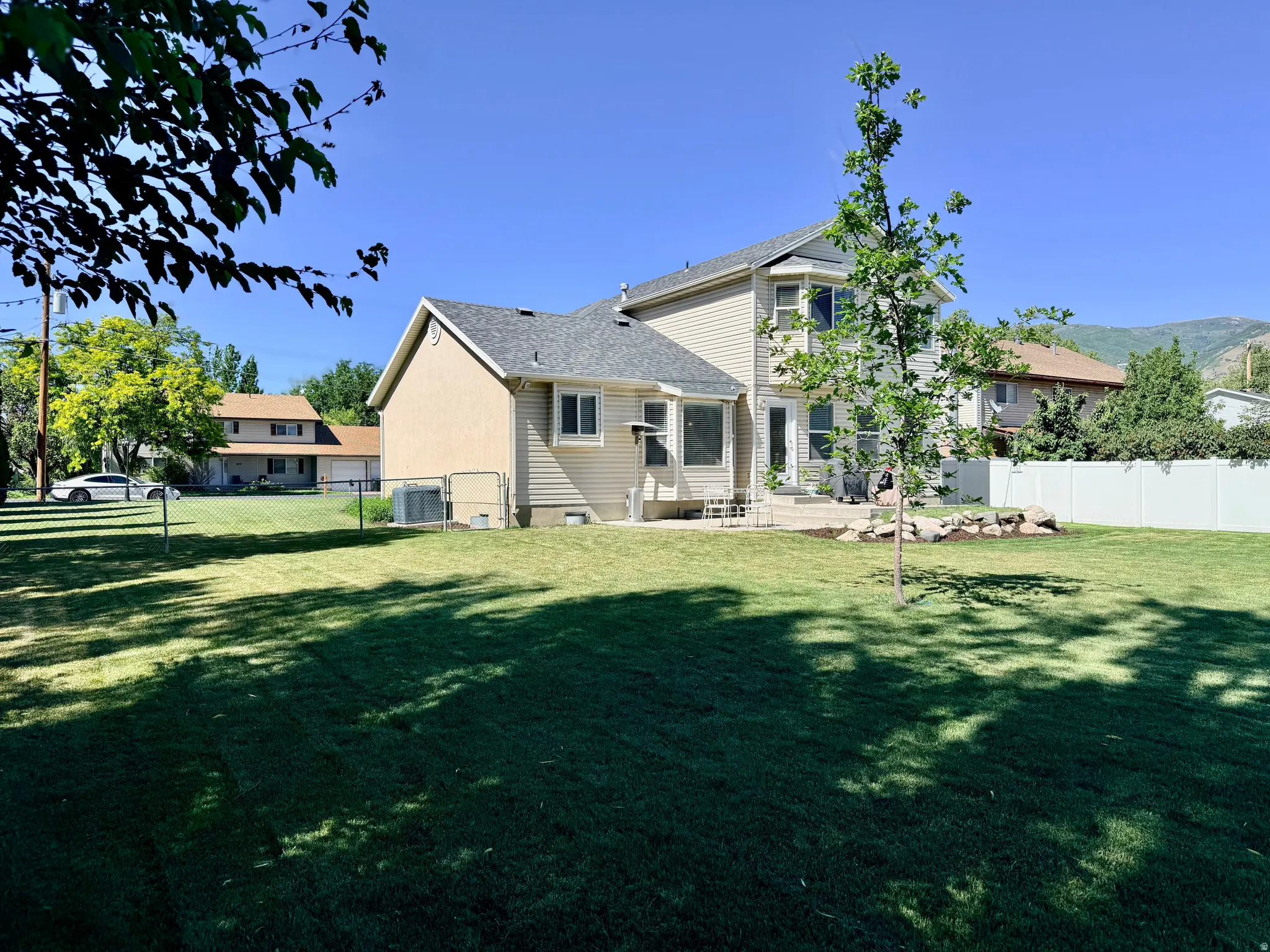 Expansive backyard featuring a manicured lawn, established landscaping, a concrete patio, a bay window, and a privacy fence