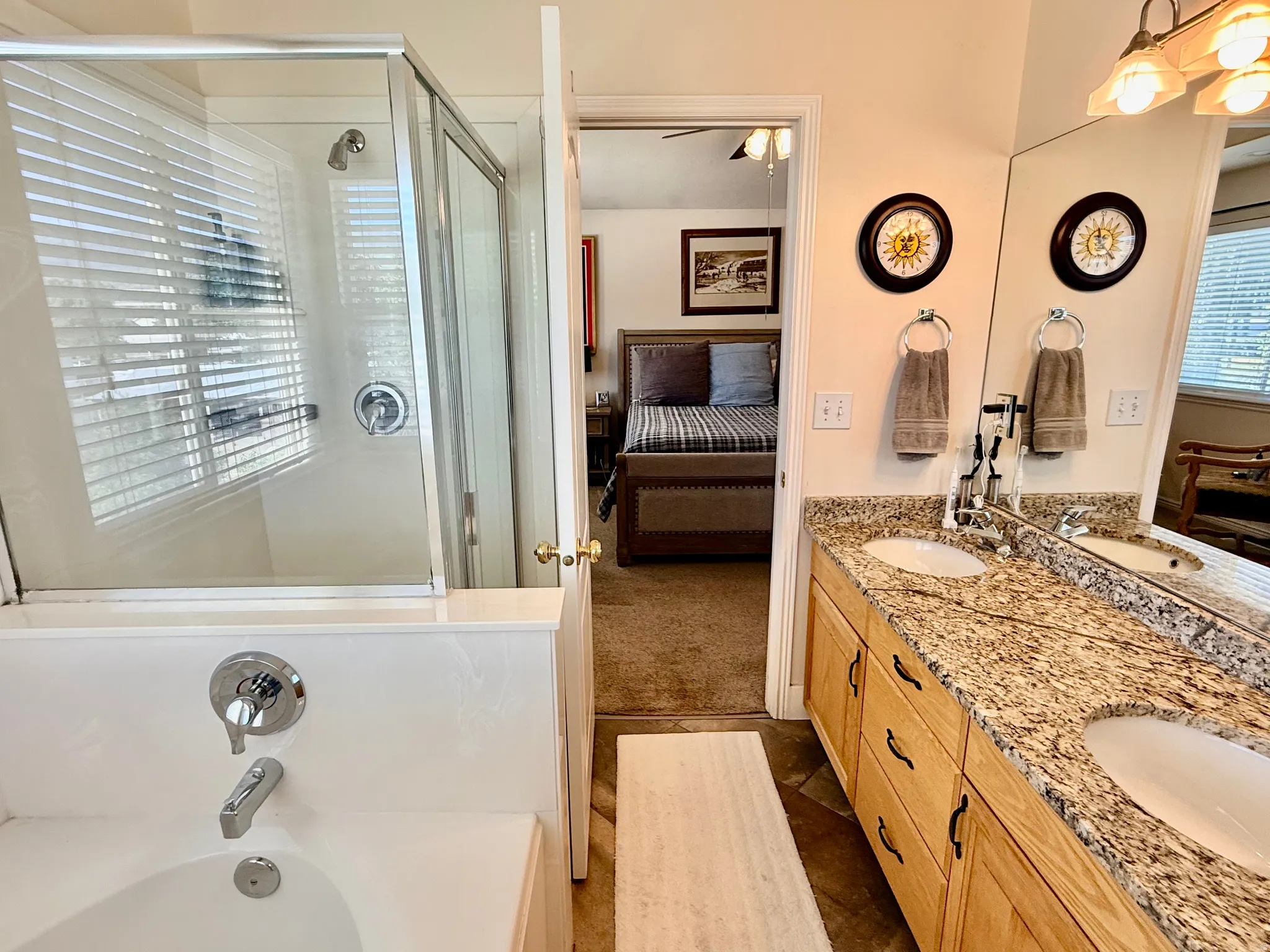 Bathroom featuring a dual-sink vanity with a stone-finish countertop, wood cabinetry, and a mirrored wall