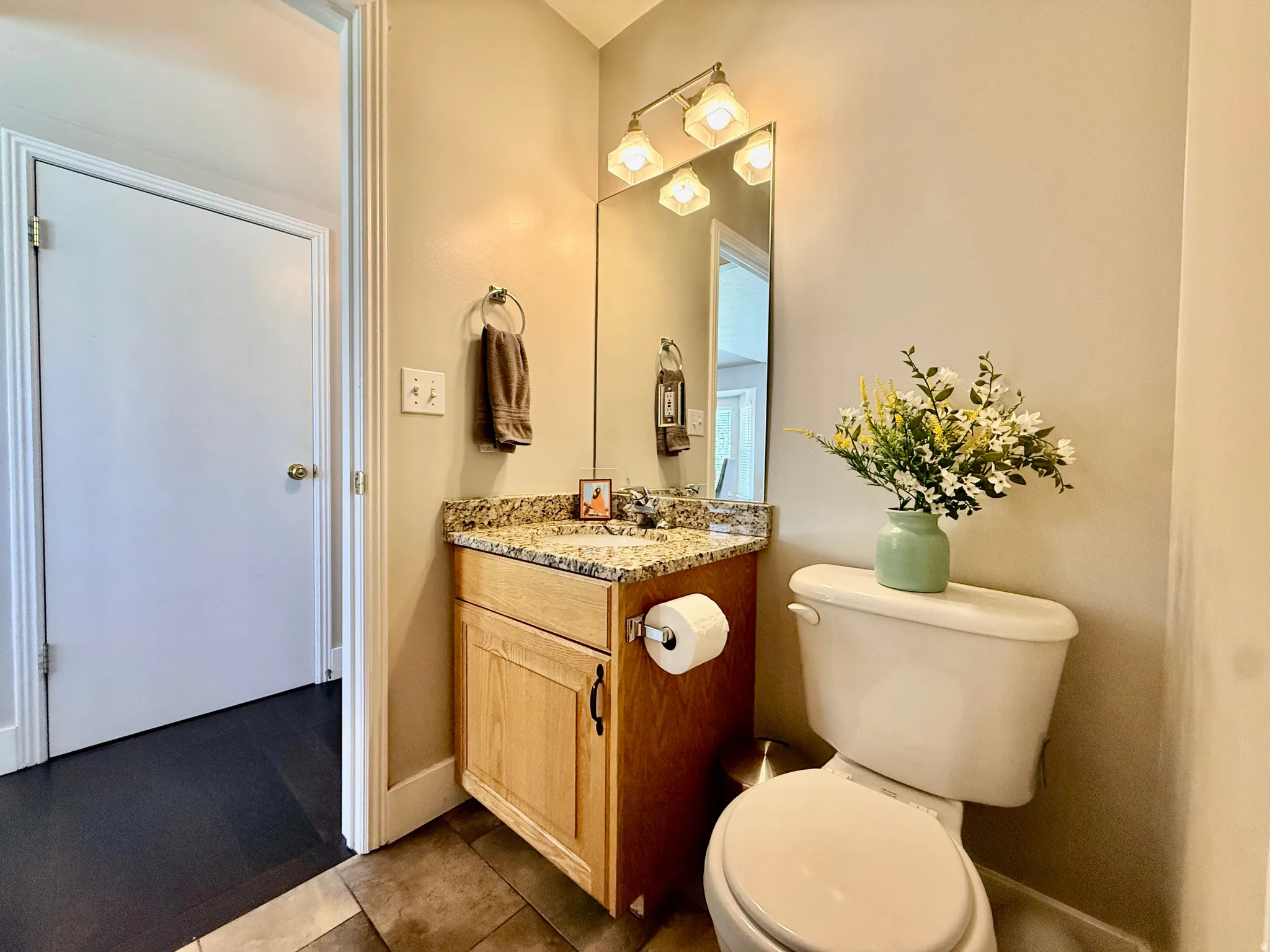 Powder room featuring a light wood-finish vanity with a granite countertop, undermount sink, and a framed mirror with overhead lighting