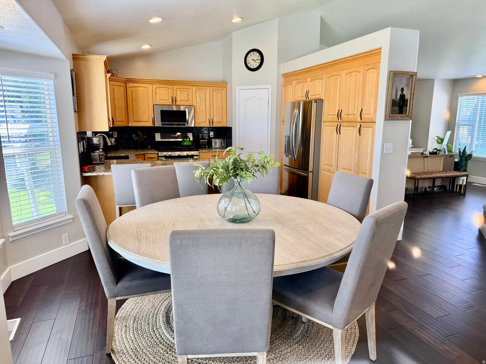 Kitchen and dining area featuring vaulted ceilings, recessed lighting, wood-finish flooring, light wood cabinetry, and stainless steel appliances