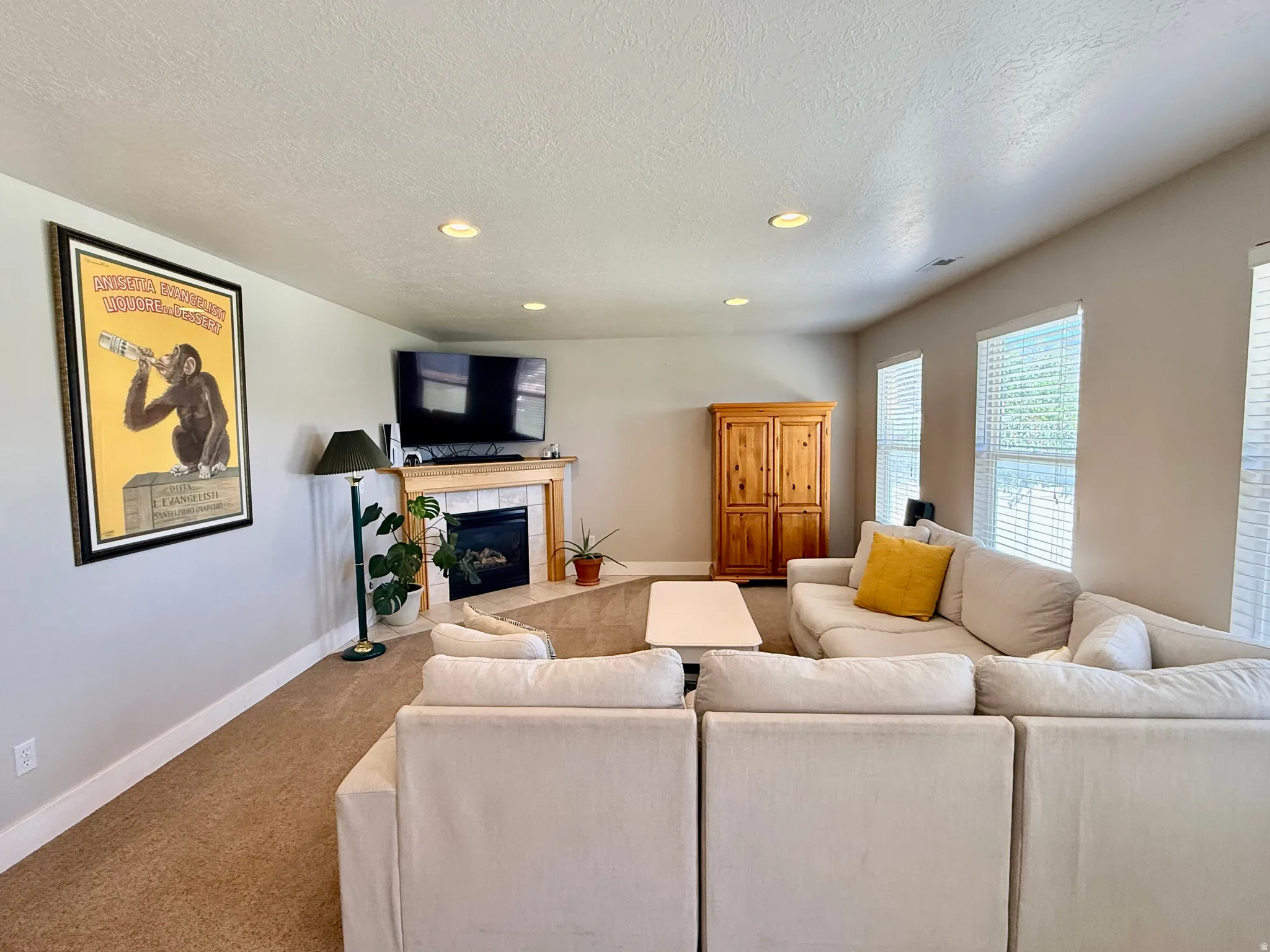 Living space featuring a fireplace with a light wood mantel and tile surround, recessed lighting, and multiple windows with blinds