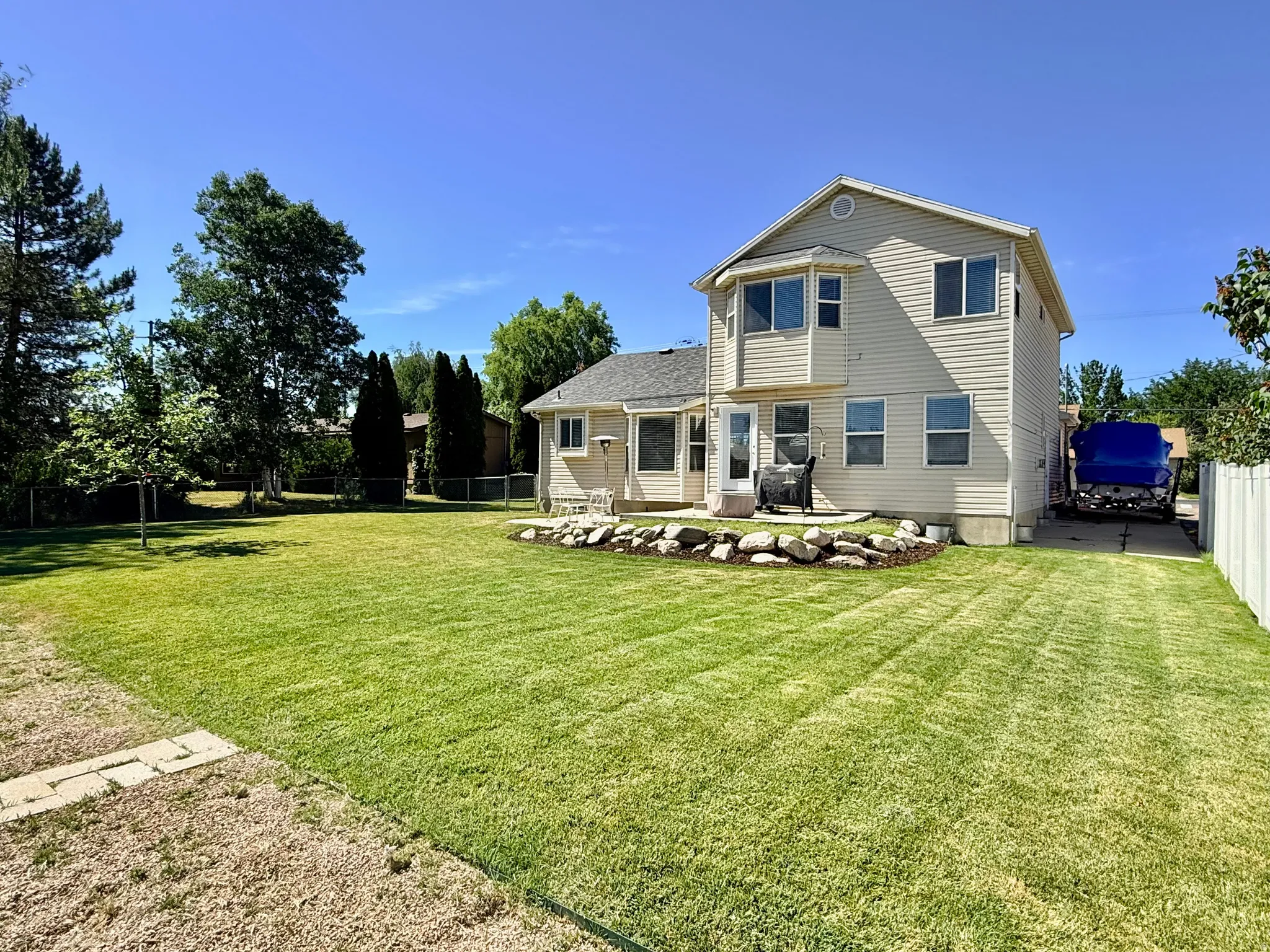 Expansive backyard featuring a manicured lawn, established trees, and a patio area