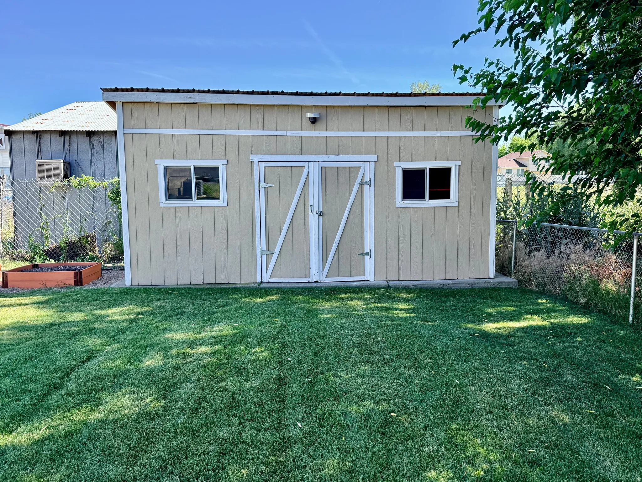 Exterior storage shed with a metal roof, two windows, double barn-style doors, and a neutral-toned siding finish