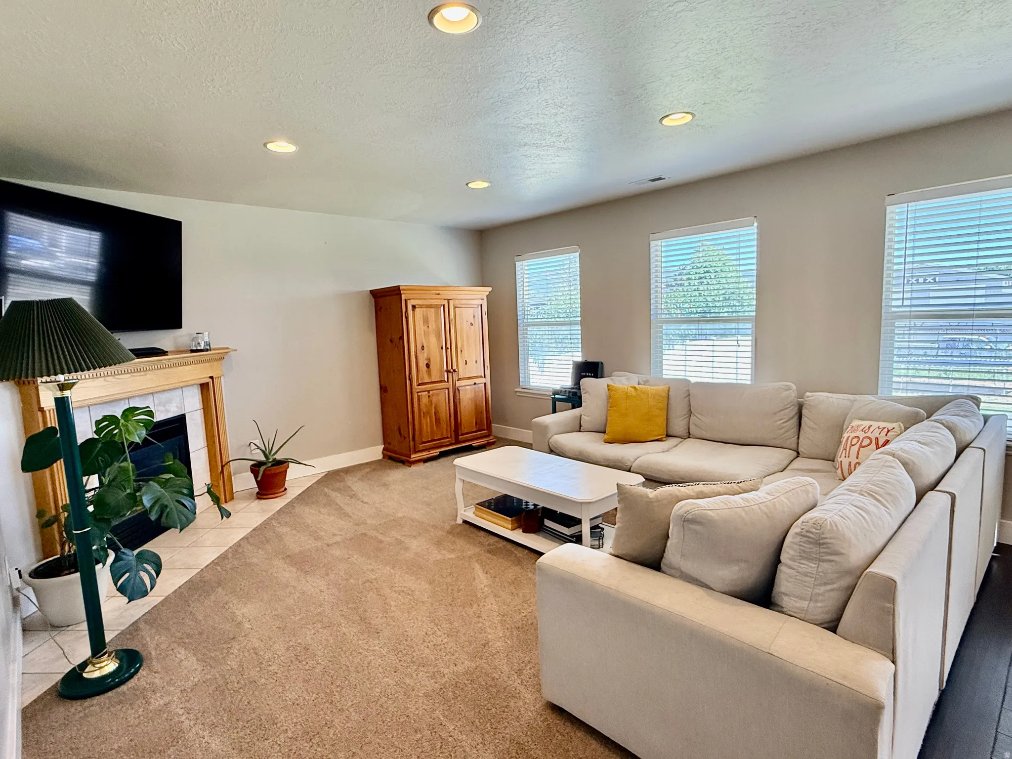 Living space featuring recessed lighting, a fireplace with a light wood mantel and tile surround, multiple windows with blinds, and carpet flooring