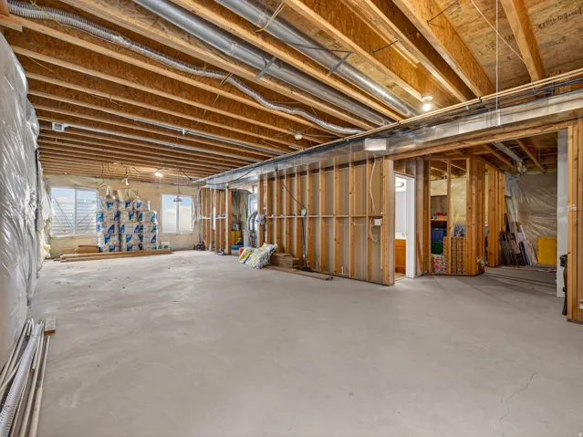Unfinished basement presenting exposed ceiling joists, visible ductwork, and concrete flooring