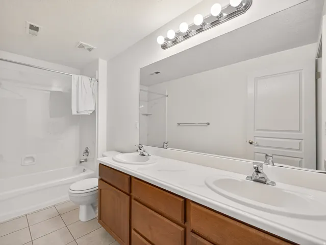 Bathroom featuring a dual-sink vanity with wood-finish cabinetry, a large wall-mounted mirror, and a combined shower-bathtub unit