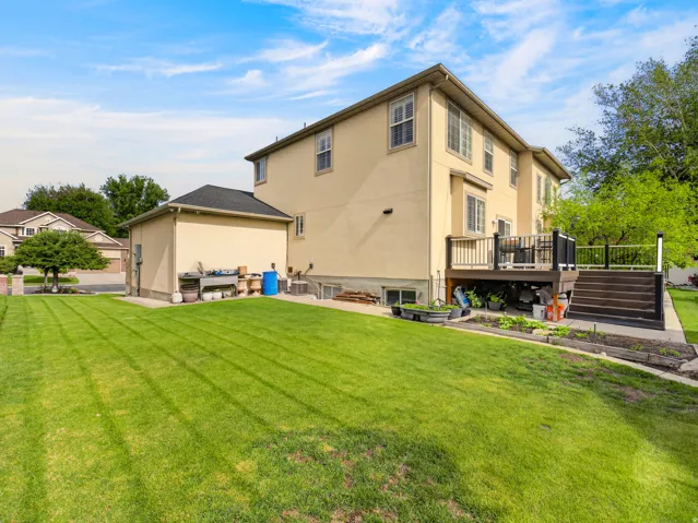 Expansive backyard featuring a manicured lawn, a multi-level deck with dark wood-finish steps and black railings, and a stucco exterior