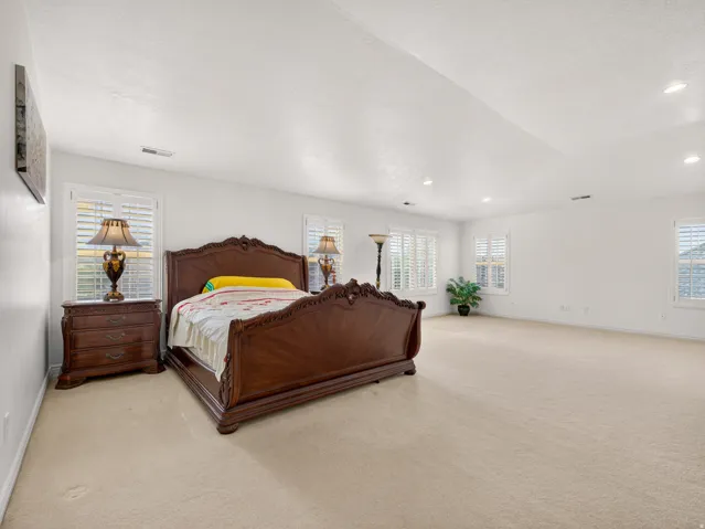 Spacious bedroom featuring light-colored carpet flooring and multiple windows with white plantation shutters