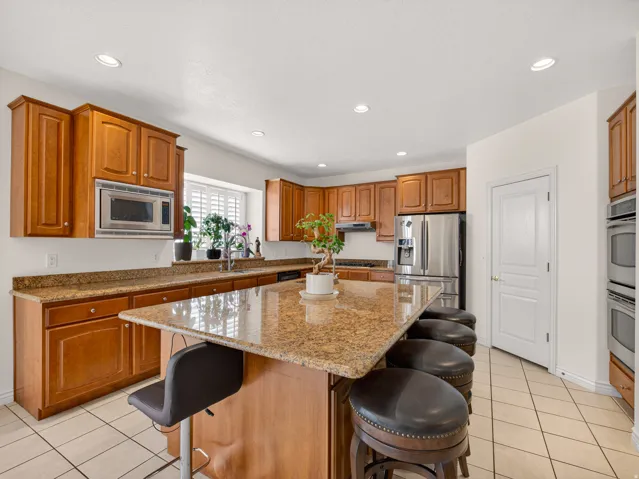 Kitchen featuring a large central island with a stone-finish countertop, wood-finish cabinetry, stainless steel appliances, recessed lighting, and tile flooring