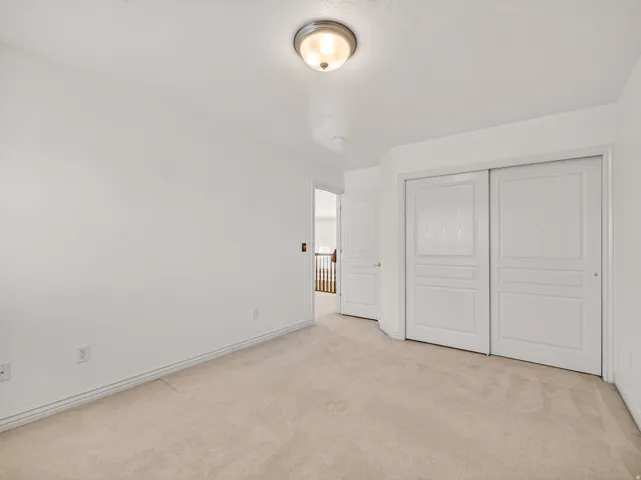 Beige carpeting throughout, featuring white baseboards, white walls, and a flush mount ceiling light fixture