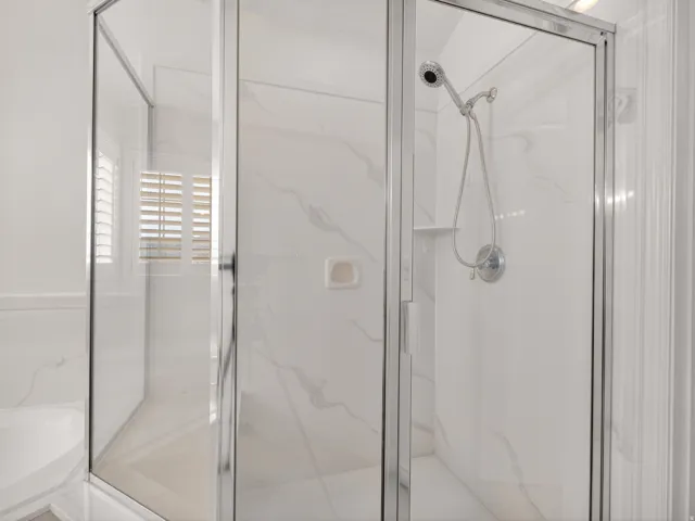 Glass-enclosed shower with a handheld showerhead and wall-mounted fixture