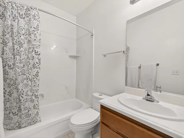 Bathroom featuring a white tub and shower surround, a single vanity with wood-finish cabinetry and an integrated sink, and a wall-mounted mirror