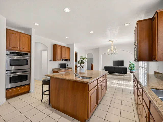Spacious kitchen featuring a central island with a built-in sink, granite countertops, wood cabinetry, and stainless steel double ovens