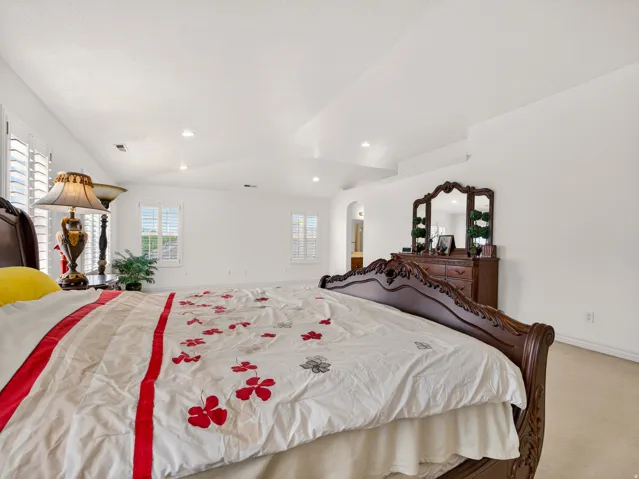 Spacious room featuring vaulted ceilings, recessed lighting, white walls, and plantation shutters on multiple windows
