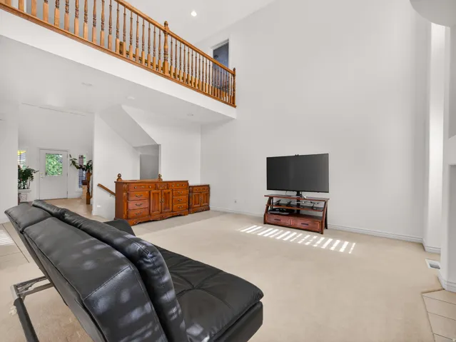 Expansive living area featuring a two-story ceiling, upper-level wood spindle railing, neutral carpeting, and a white entry door with glass panels