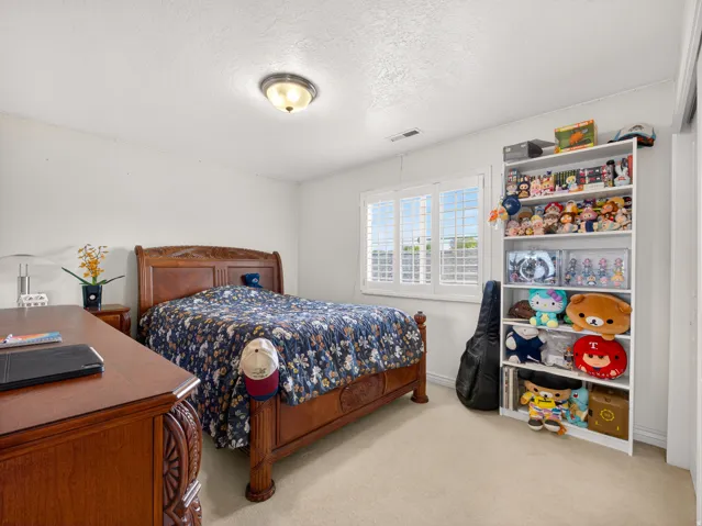 Carpeted room featuring a window with plantation shutters, a ceiling-mounted light fixture, and a built-in shelving unit