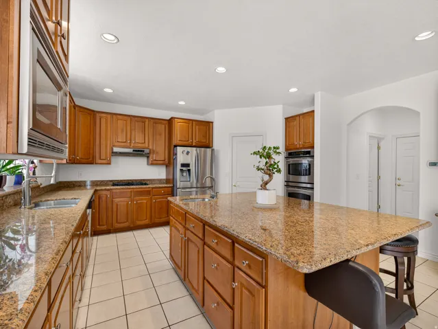 Spacious kitchen featuring an expansive island, stone countertops, wood cabinetry, stainless steel appliances, and tile flooring