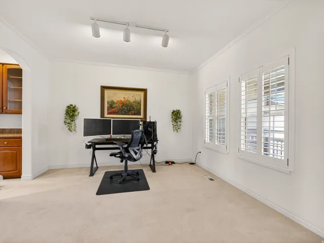 Carpeted room featuring two windows with white plantation shutters, crown molding, and recessed track lighting