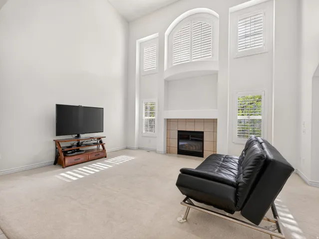 Two-story living area featuring a fireplace with tile surround, arched window with plantation shutters, and additional windows with plantation shutters