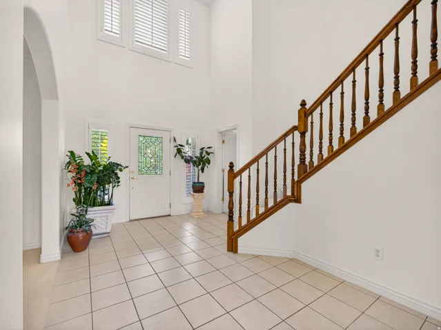 Two-story entryway featuring a wood staircase with turned balusters, a front door with leaded glass, tile flooring, and arched entryway