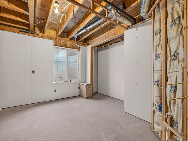 Unfinished basement space with exposed wooden joists and ductwork, featuring a concrete floor, framed walls with drywall, and a horizontal window
