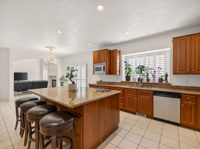 Kitchen featuring a granite-topped island with seating, warm wood cabinetry, and a stainless steel dishwasher