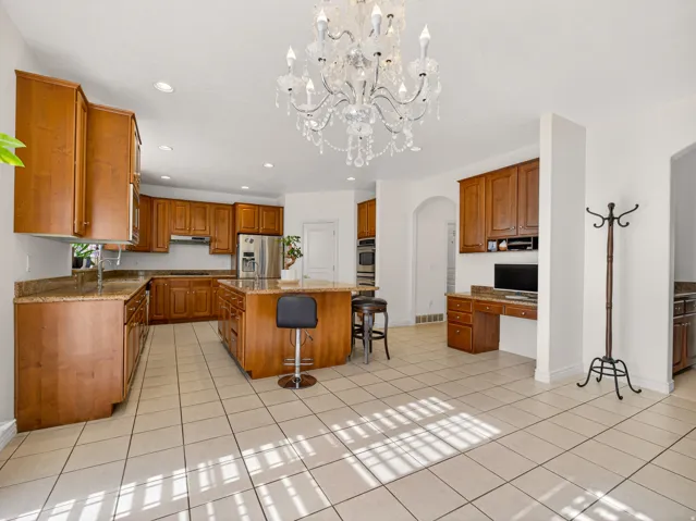 Spacious kitchen featuring extensive wood cabinetry, light-toned tiled flooring, and granite countertops