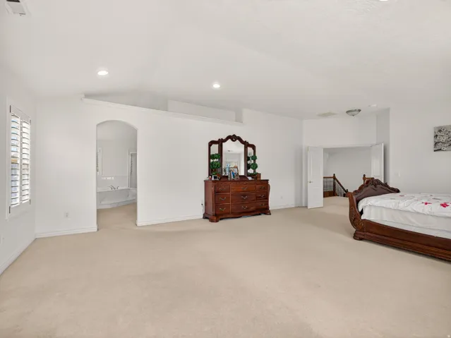 Spacious room featuring neutral carpet flooring, recessed lighting, white louvered window shutters, and an arched doorway leading to a built-in tub