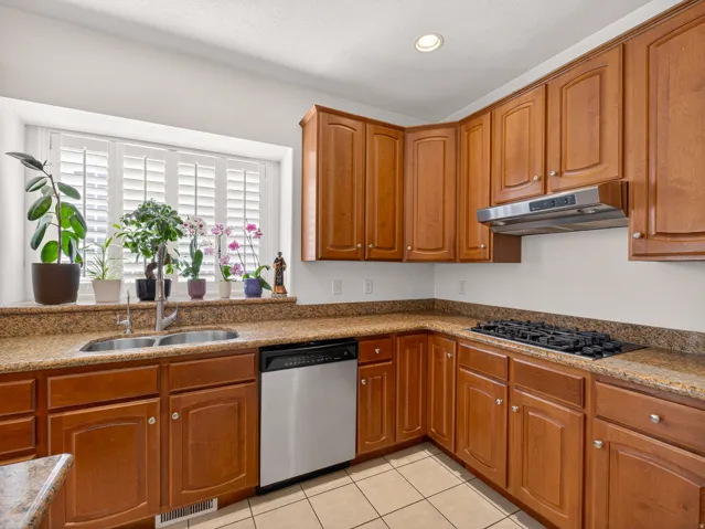 Kitchen featuring wood cabinetry, granite countertops, a stainless steel double basin sink, a gas cooktop with an overhead range hood, and tile flooring