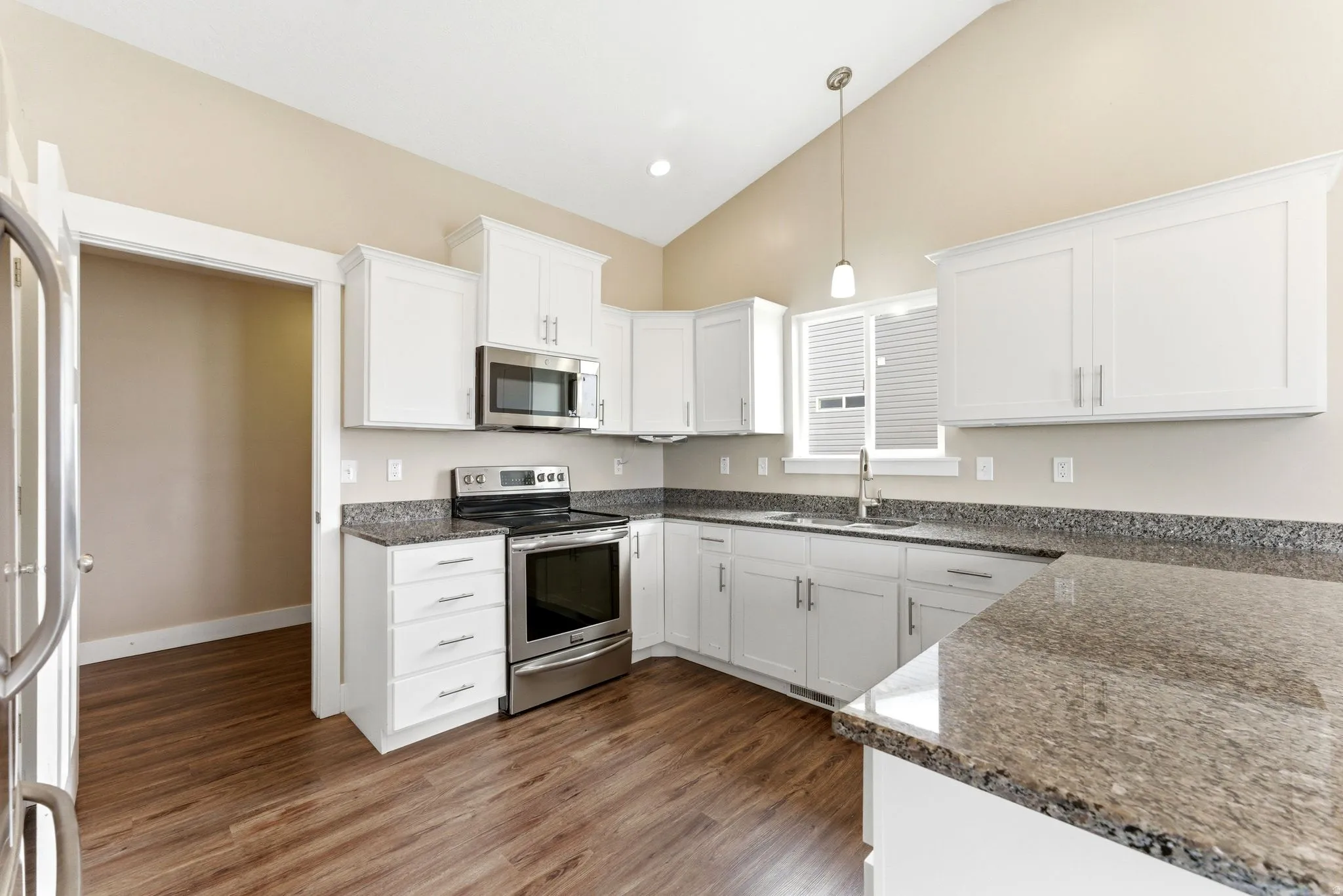 Kitchen featuring vaulted ceilings, white shaker-style cabinetry, stainless steel appliances, granite countertops, and wood-finish flooring