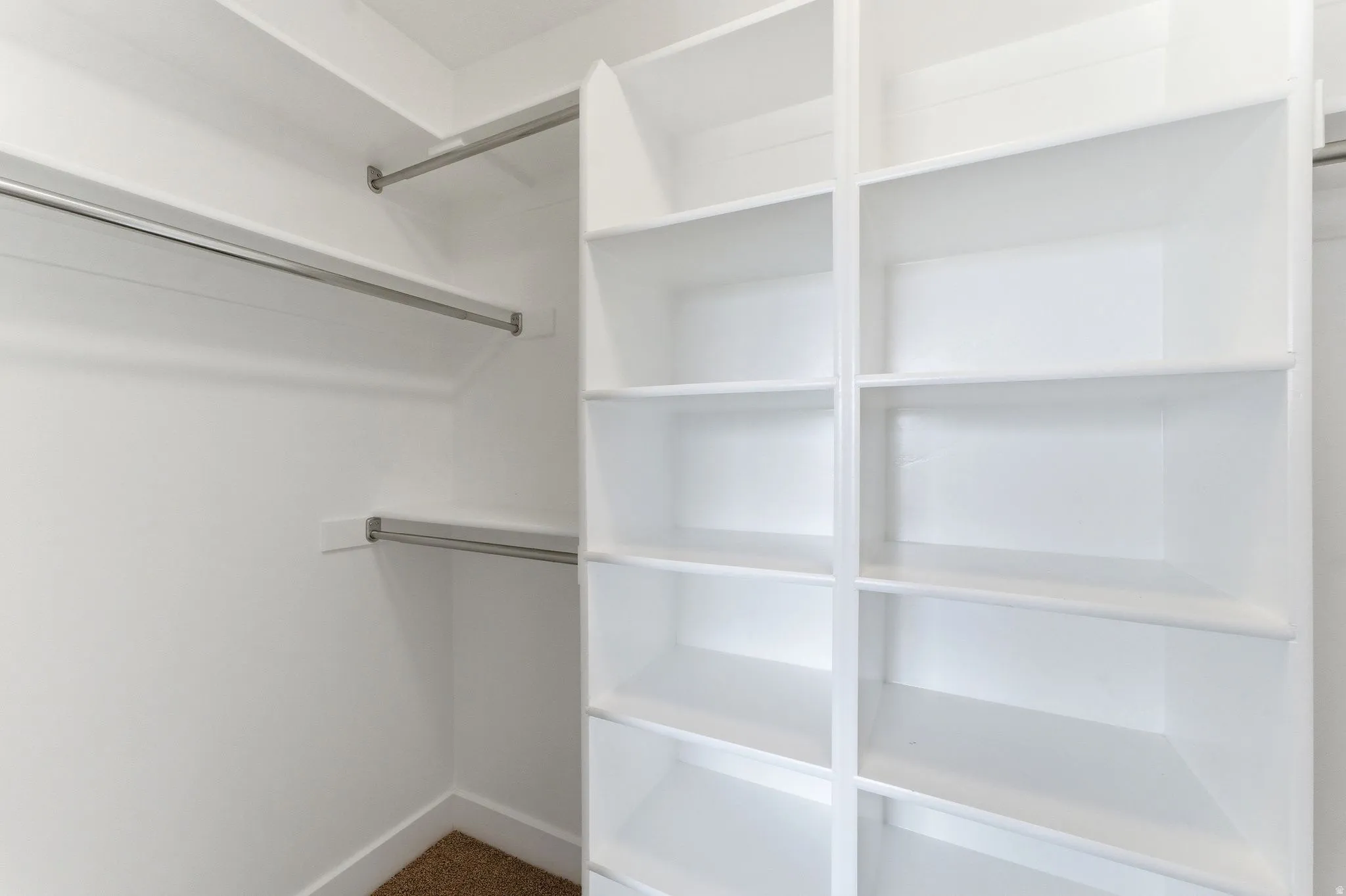 Built-in closet organization system featuring white shelving units, multiple clothing rods, and wall-to-wall carpeting