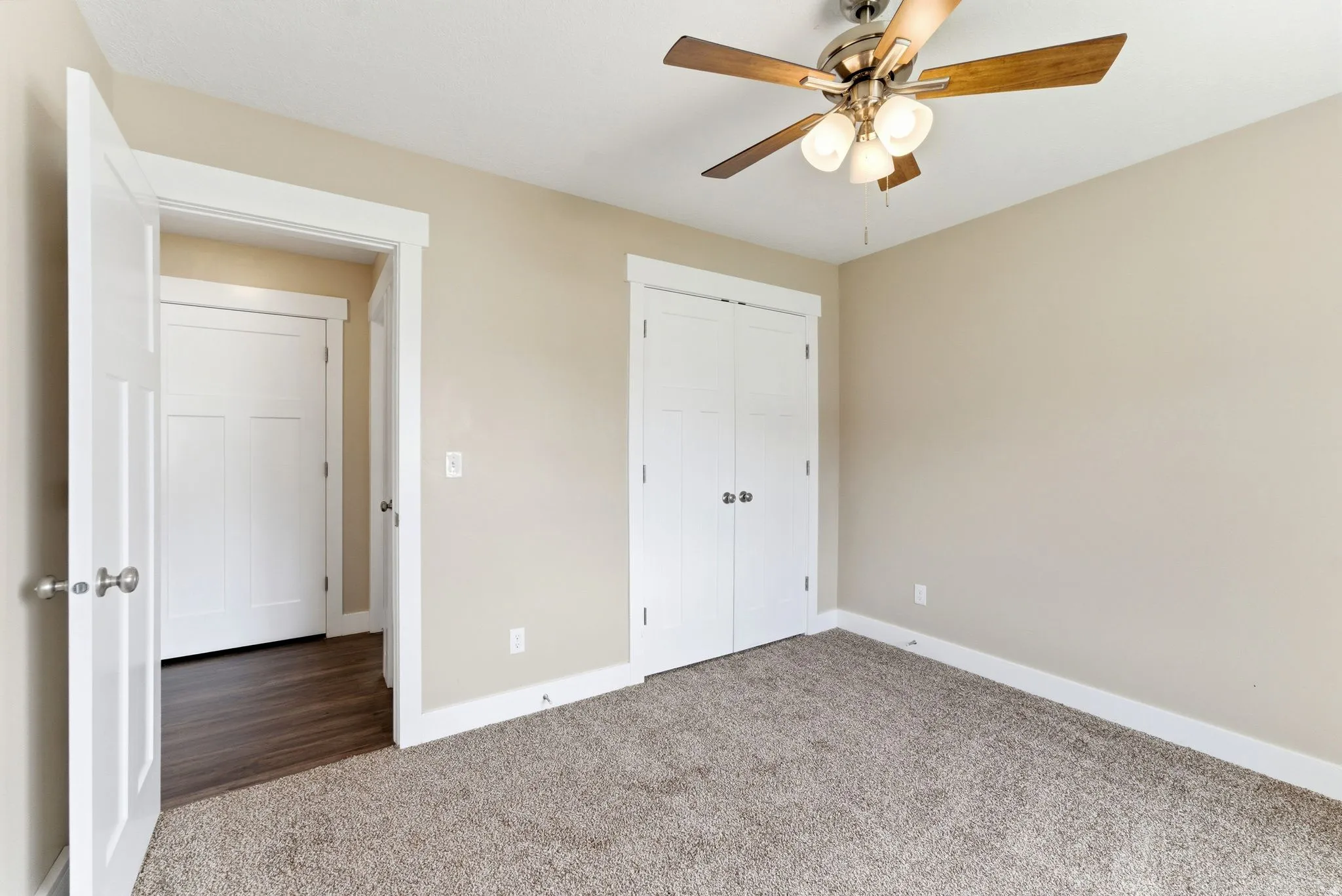 Neutral-toned room featuring plush carpeting, a ceiling fan with light fixture, and wide white baseboards