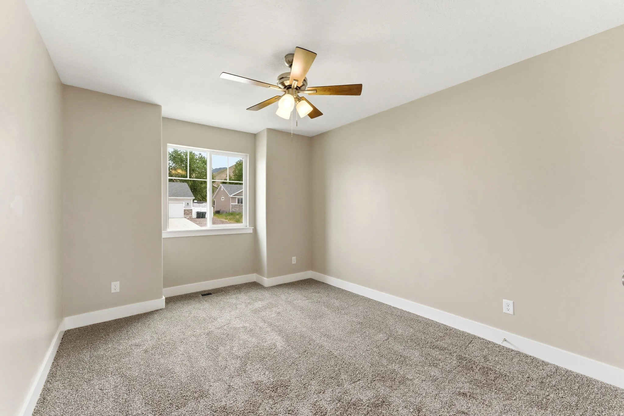 Spacious room featuring neutral-toned walls, plush carpet flooring, a multi-pane window with white trim, and a ceiling fan with integrated lighting