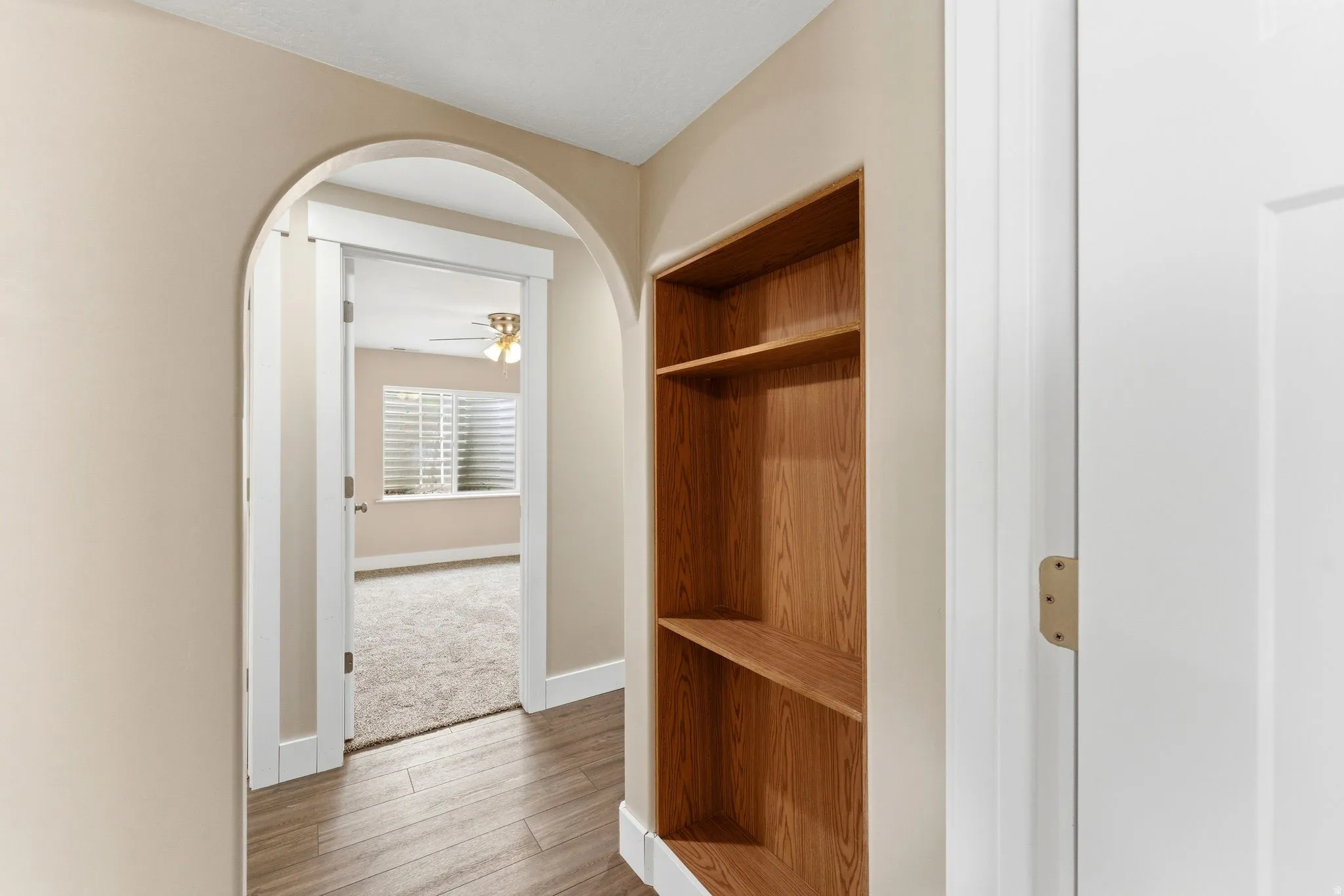 Arched entryway leading to a room with plush carpet, plantation shutters, and a ceiling fan