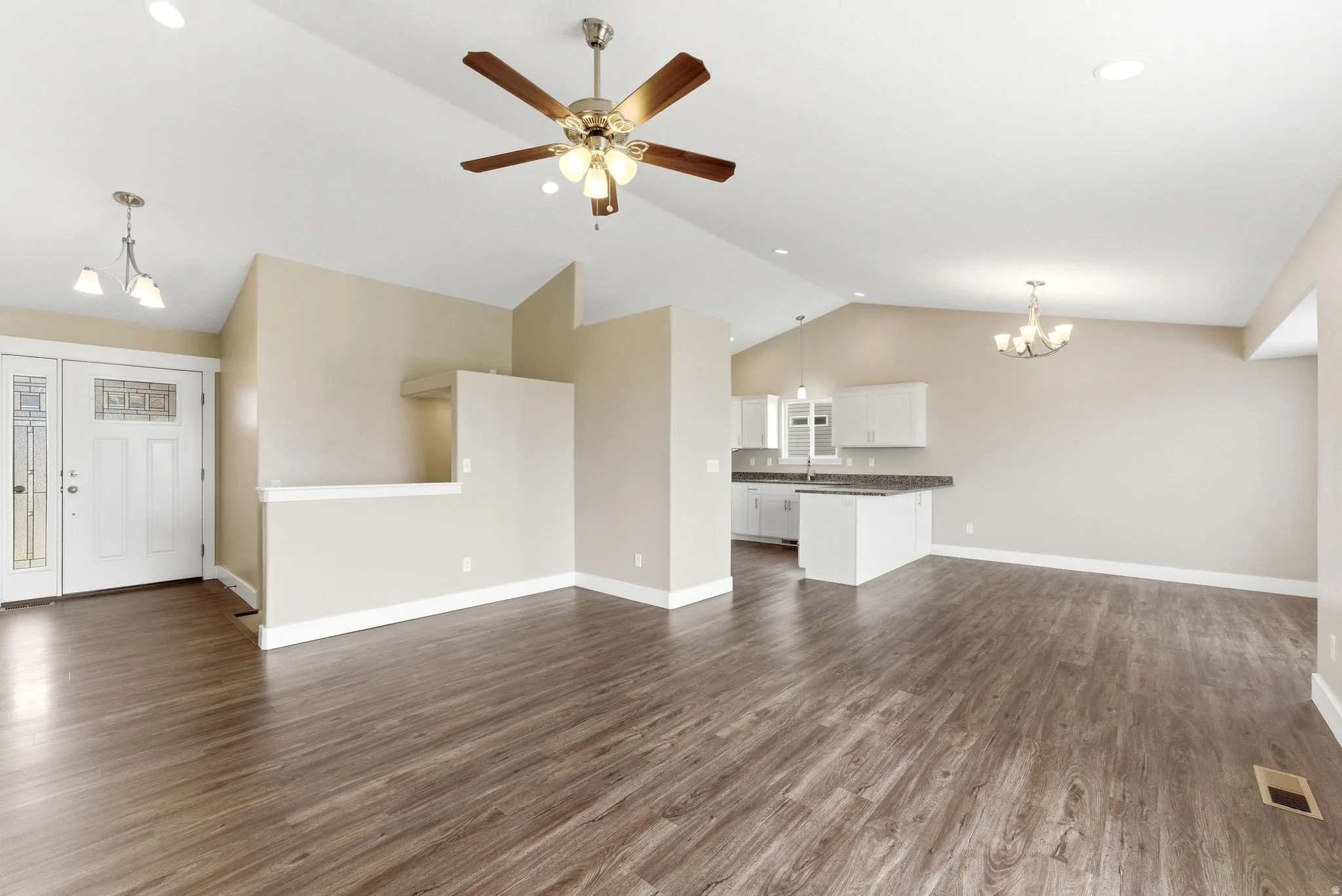 Spacious open-concept living area featuring wood-finish flooring, vaulted ceilings, a ceiling fan, and recessed lighting