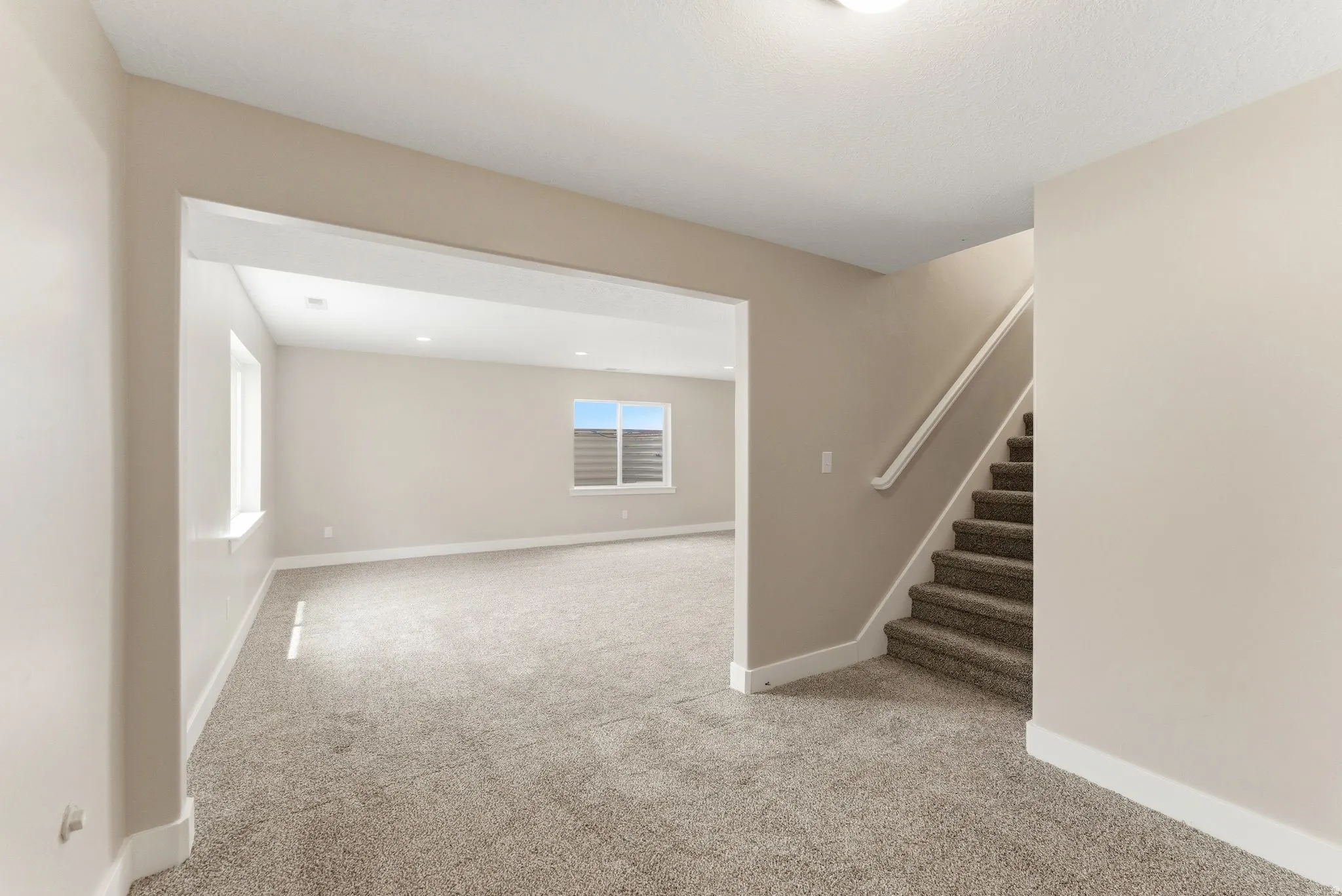 Spacious interior featuring neutral carpeting, light-toned walls, recessed lighting, and a prominent staircase with a white handrail