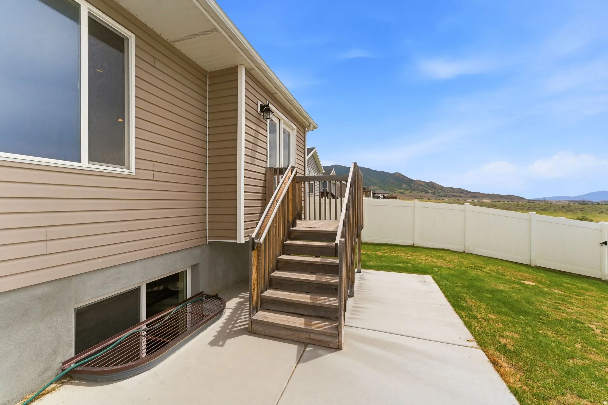 Rear exterior featuring horizontal siding, a wooden deck and staircase, concrete patio, and a white privacy fence