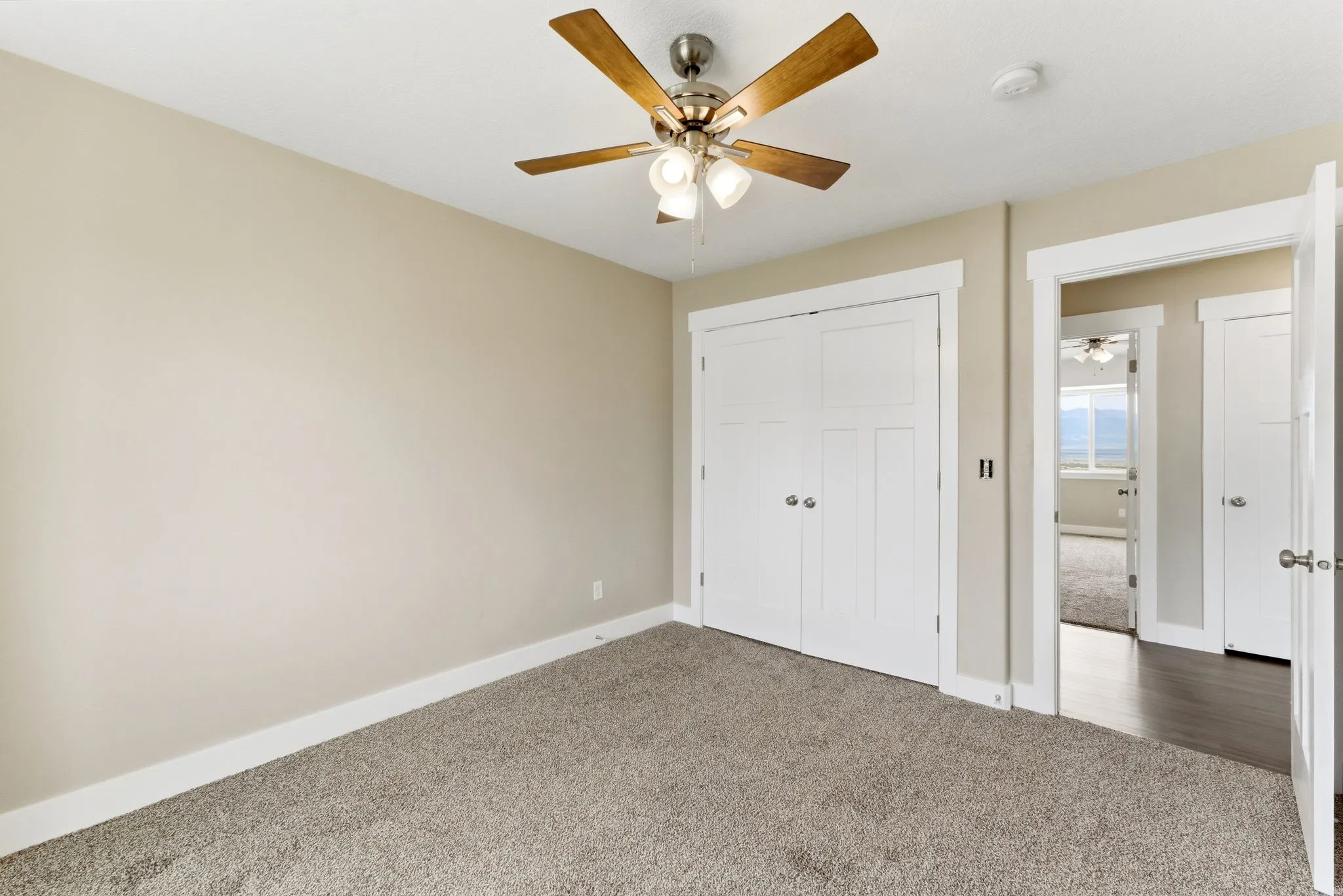 Carpeted interior space featuring an overhead ceiling fan, neutral wall paint, white trim, and a double-door closet with contrasting hardware